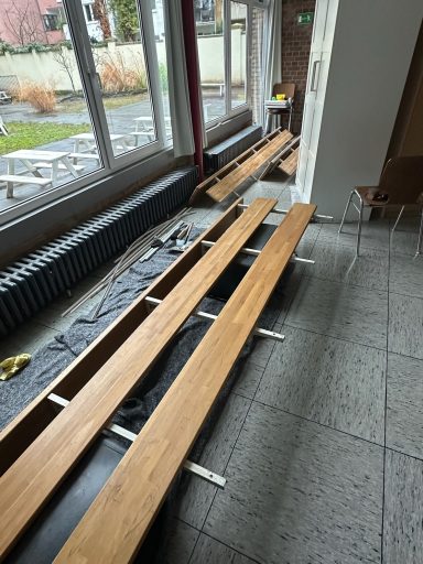 Holztische liegen auf einem Boden in einem Raum mit großen Fenstern.